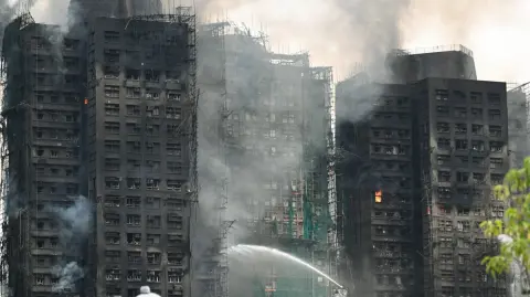 Los bomberos rocían agua sobre las llamas mientras un gran incendio quema varios bloques de apartamentos en el complejo residencial Wang Fuk Court en el distrito Tai Po de Hong Kong