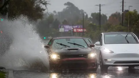 Un automóvil circula por una carretera inundada en el bulevar La Cienega el 24 de diciembre de 2025 en Los Ángeles, California.
