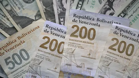(FILES) Picture of Venezuelan bolivar and US dollar bills taken in Caracas on September 30, 2025. On December 31, 2025, the Central Bank of Venezuela (BCV) valued the dollar at 301.37 bolivars (Venezuelan currency), a price valid until January 2, representing an increase of 479.25% compared to the 52.02 bolivars set by the issuing entity at the beginning of 2025. (Photo by Federico PARRA / AFP)