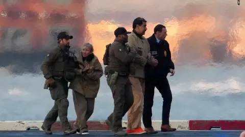 Las autoridades sacan del helicóptero al presidente venezolano Nicolás Maduro y a su esposa Cilia Flores, mientras Maduro se dirige al juzgado Daniel Patrick Moynihan de Estados Unidos en Manhattan