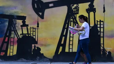 Una mujer pasa junto a un mural que representa una bomba de petróleo en una calle de Caracas.