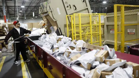 LOS ANGELES, CALIFORNIA - DECEMBER 02: A U.S. Postal Service employee sorts packages during the start of the holiday mail rush, following Black Friday and Cyber Monday, inside the Los Angeles Mail Processing & Distribution Center on December 2, 2025 in Los Angeles, California. The 1.7 million square foot facility, the largest in the United States, is currently processing around one million packages per day as the Postal Service enters its busiest part of the year amid the December holiday season leading up to Christmas.   Mario Tama/Getty Images/AFP (Photo by MARIO TAMA / GETTY IMAGES NORTH AMERICA / Getty Images via AFP)
