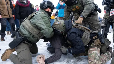 Agentes federales derriban a un manifestante al suelo antes de detenerlo afuera del edificio federal Whipple.