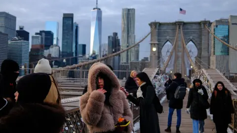 People brave the cold temperatures while walking on the Brooklyn Bridge in the Manhattan borough of New York City on January 21, 2026. Bringing icy temperatures, Winter Storm Fern will slam a massive stretch of the United States this week, with more than 175 million people facing the prospect of heavy snowfall, power outages and travel disruption. Forecasters warned it could be 2,000 miles (3,219 kilometers) long, well over half the length of the continental US. (Photo by CHARLY TRIBALLEAU / AFP)