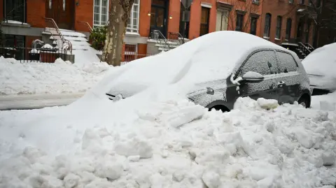 A car is plowed in with snow a day after a winter storm swept through the region in the Brooklyn borough of New York City on January 26, 2026. A monster storm barreling across the United States had killed at least 11 people on Monday, prompting warnings to stay off the roads, mass flight cancelations and power outages after a weekend of misery. The storm dumped snow, sleet and freezing rain across swathes of the country from Texas to New England, with temperatures set to fall dangerously low this week. (Photo by ANGELA WEISS / AFP)