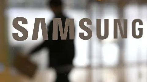 A man walks past the logo of Samsung Electronics displayed on a glass door at the company's Seocho building in Seoul on January 29, 2026. South Korean tech giant Samsung Electronics posted record quarterly profits on January 29, riding strong market demand for its artificial intelligence chips. (Photo by Jung Yeon-je / AFP)