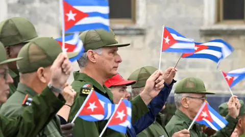 El presidente de Cuba, Miguel Díaz-Canel (centro), ondea una bandera cubana.