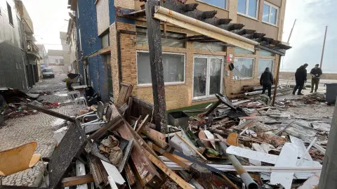 La gente camina entre escombros en una calle de Praia da Vieira, después de que la tormenta Kristin azotara Portugal.