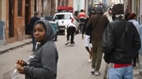 A bundled-up woman stands in a street in Havana on February 3, 2026. Cuba registered a record low of zero degrees on February 3 the first time freezing point has been documented on the Caribbean island, according to its Institute of Meteorology. (Photo by YAMIL LAGE / AFP)