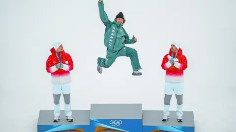 Brazil's gold medalist Lucas Pinheiro Braathen (C) leaps onto the podium flanked by Switzerland's silver medalist Marco Odermatt (L), and Switzerland's bronze medalist Loic Meillard during the podium of the men's giant slalom alpine skiing event during the Milano Cortina 2026 Winter Olympic Games at the Stelvio Ski Centre in Bormio (Valtellina) on February 14, 2026. (Photo by Fabrice COFFRINI / AFP)