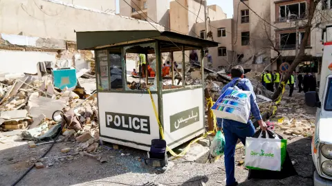 Hombre iraní con bolsas mientras camina entre los escombros.