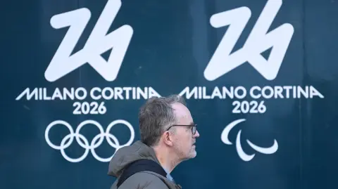 Un hombre pasa junto al logo de los Juegos Olímpicos y Paralímpicos Milán-Cortina 2026 en Milán.