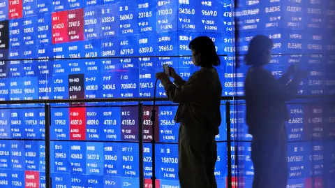 Un visitante se encuentra junto a una pantalla electrónica que muestra el tablero de cotización de los precios de las acciones Nikkei de Japón dentro de una sala de conferencias en Tokio, Japón.