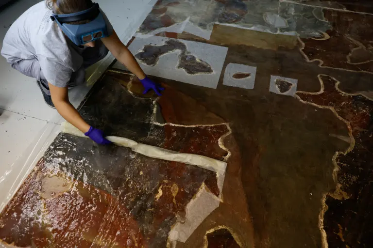 Un técnico de conservación y restauración retira la emulsión de disolvente gelificado durante el proceso de biolimpieza de un panel con una pintura mural retirada de la iglesia de Santos Juanes.
