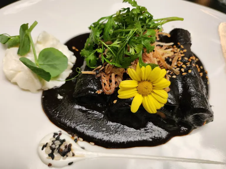Enchiladas de Mole Negro, rellenas de plátano macho con almendras y nuez de la India, y coronadas con una nube de queso cuadro chiapaneco.