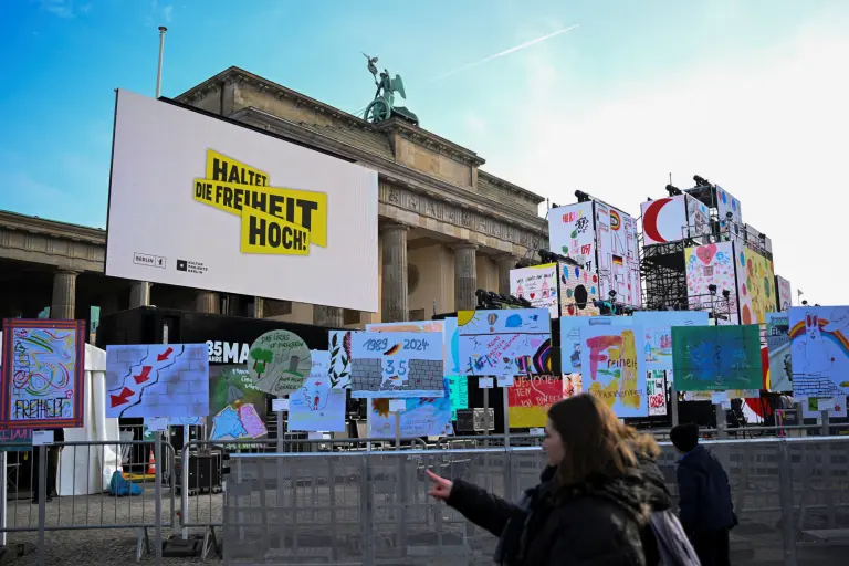 La gente avanza junto a una instalación al aire libre con carteles y carteles a lo largo del camino del antiguo Muro de Berlín en el 35º aniversario de la caída del Muro en Berlín, Alemania.