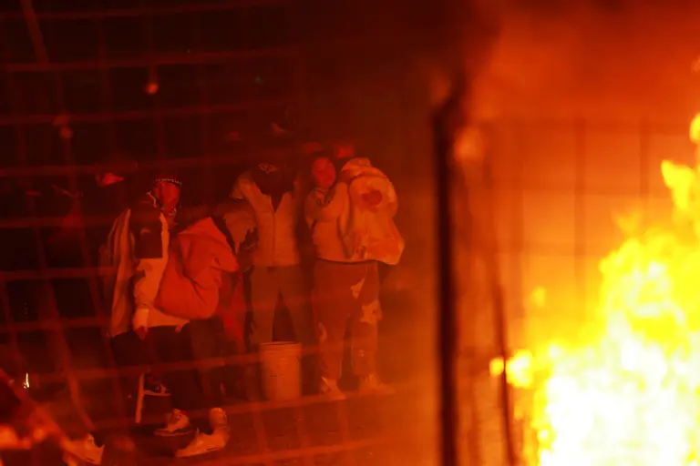 Migrantes reaccionan durante un operativo de desalojo realizado por autoridades mexicanas, mientras el campamento improvisado donde vivían se incendia, en Chihuahua, estado de Chihuahua.