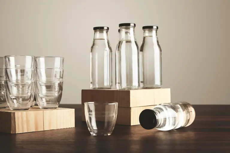 Perfect set of pure clean healthy water in transparent glass bottles and cups presented on wooden plates on tableOne cup and bottle in front close up