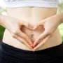 Close-up of female hands shaping heart on belly outdoors. Fitness and dieting concept